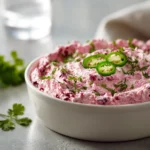 Close-up of baked cranberry cream cheese dip with jalapeños, topped with fresh herbs and served with crackers.