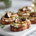 Close-up of Brie, Apple & Fig Crostini topped with honey and thyme, served on a modern white platter.