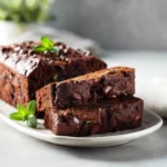 Moist zucchini brownie bread with chocolate chips, sliced on a white plate.