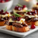 Crostini topped with smoked beef, brie, and cranberry sauce, served as an elegant Thanksgiving appetizer.