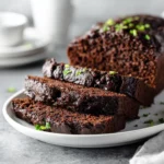 Vegan chocolate zucchini bread with walnuts and melty chocolate chips, sliced on a modern plate.