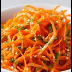 A vibrant Korean Carrot Salad with carrots, garlic, and spices in a bowl.