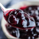 Homemade blueberry sauce drizzled over pancakes with fresh blueberries on top.