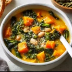 Bowl of butternut squash soup with kale and white beans garnished with herbs