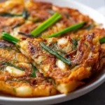Crispy Korean spring onion pancake served on a plate with dipping sauce.