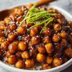 Vegan sticky sesame chickpeas on a plate garnished with sesame seeds and herbs.