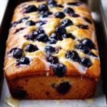 Loaf of lemon blueberry bread with fresh blueberries on a wooden table