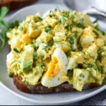 Delicious avocado egg salad served in a bowl with a sprinkle of herbs.
