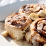 Deliciously baked banana cinnamon rolls topped with cream.