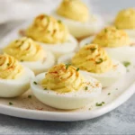 Classic deviled eggs garnished with paprika and herbs on a platter.