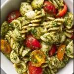 Colorful pesto pasta salad with fresh vegetables and herbs