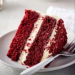 Slice of red velvet cake displayed on a plate with cream cheese frosting