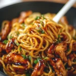 Sticky garlic chicken noodles garnished with green onions in a bowl.