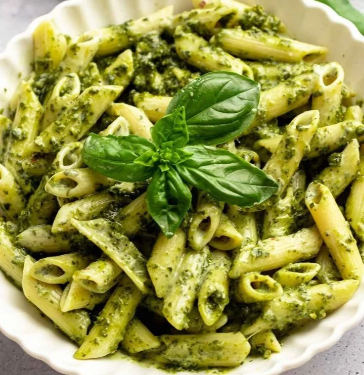 Bowl of creamy pesto pasta garnished with basil and parmesan cheese