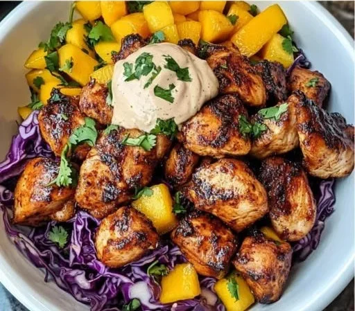 Jerk chicken and mango slaw bowls topped with honey lime cream in a vibrant presentation.