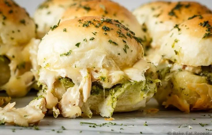 Pesto Chicken Sliders with melted cheese and fresh basil on a serving platter.