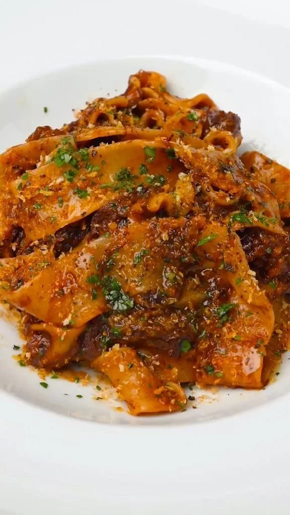 Plate of delicious braised beef pasta topped with herbs and cheese.