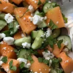 Cantaloupe melon salad with cucumber and feta cheese topped with fresh herbs.