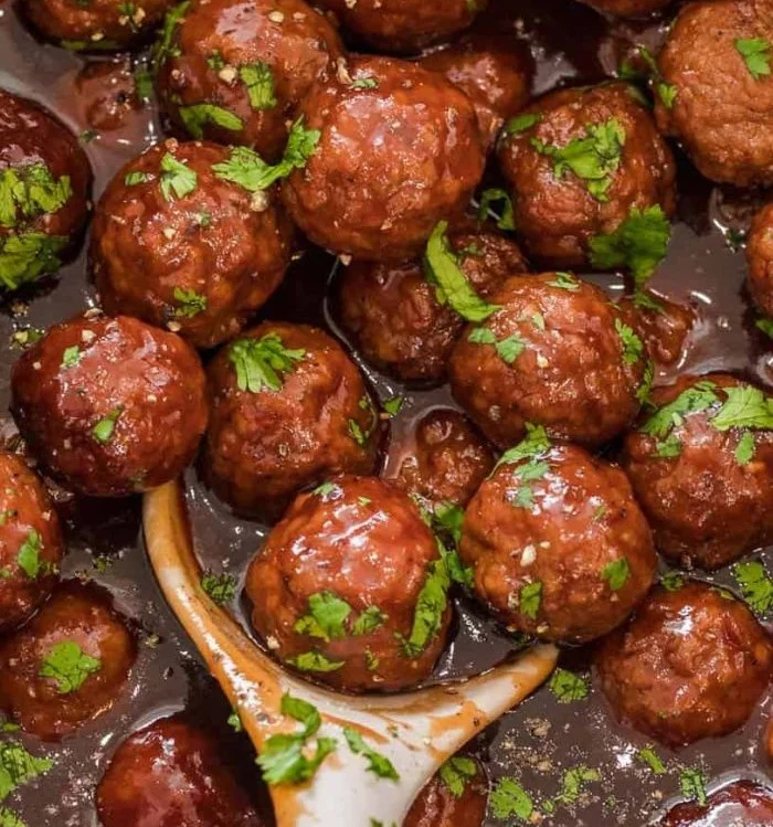 Plate of grape jelly meatballs with a garnish, served as a savory appetizer.