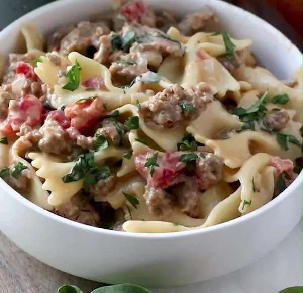 Dish of Italian sausage with bow tie pasta garnished with herbs