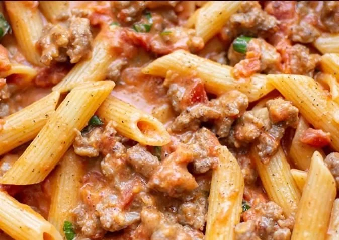 Plate of spicy Italian sausage pasta garnished with herbs