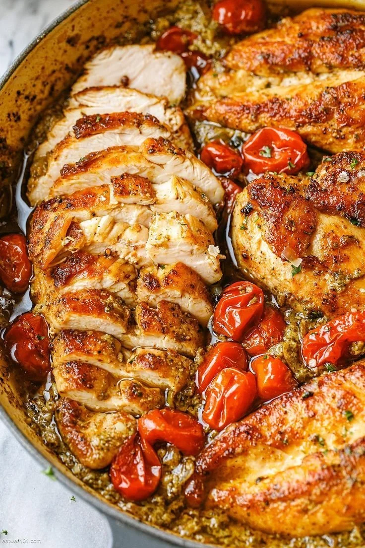 Creamy pesto chicken dish with roasted tomatoes garnished with herbs