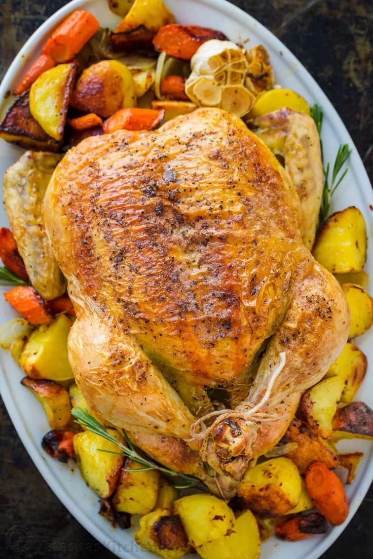 A beautifully roasted chicken with colorful vegetables on a serving plate.